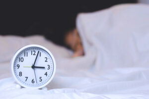 Alarm clock propped on the bed with a man asleep behind